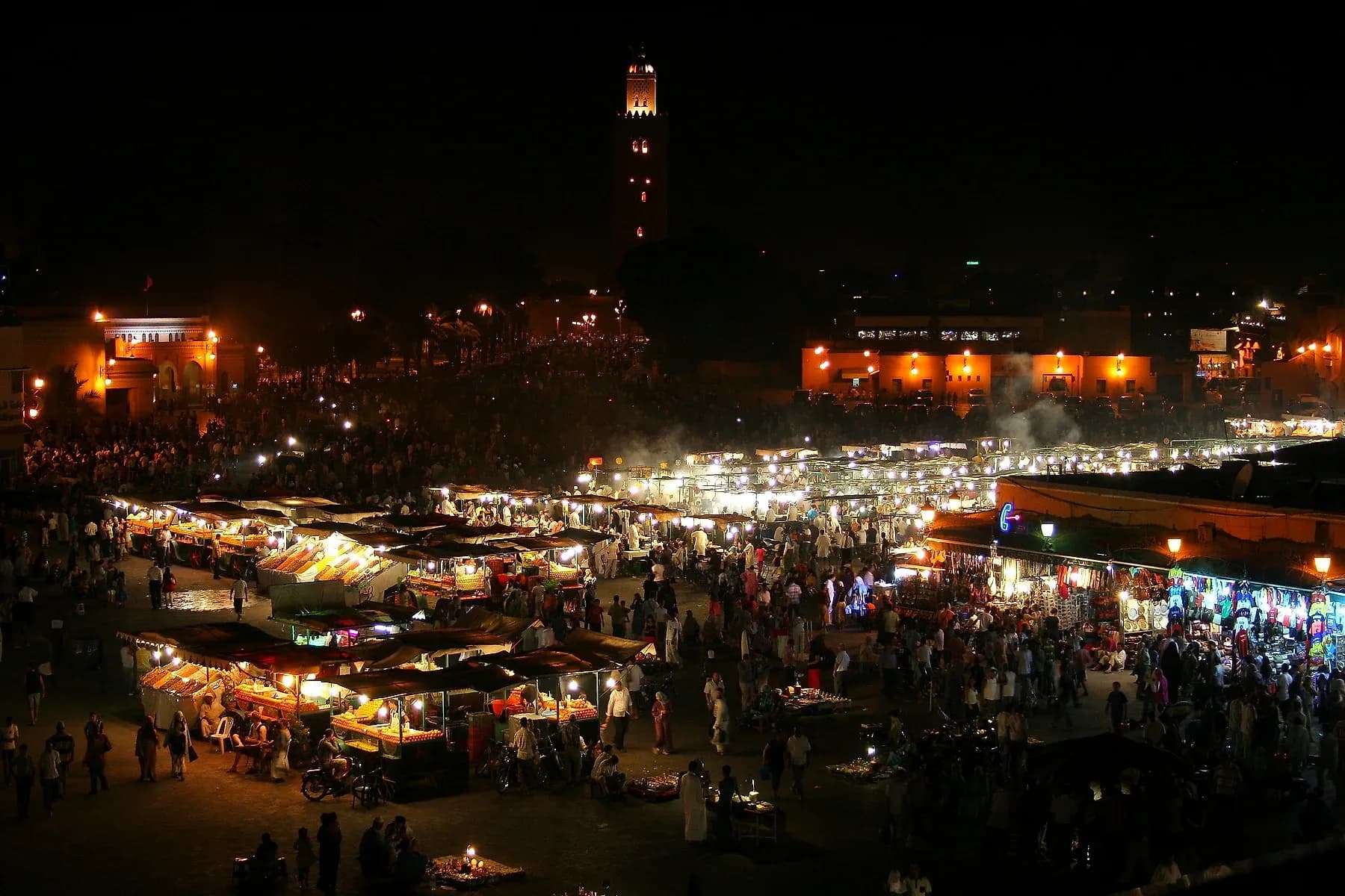 Puestos de comida iluminados en la plaza Jemaa el-Fna de noche, con la Koutoubia al fondo, Marrakech