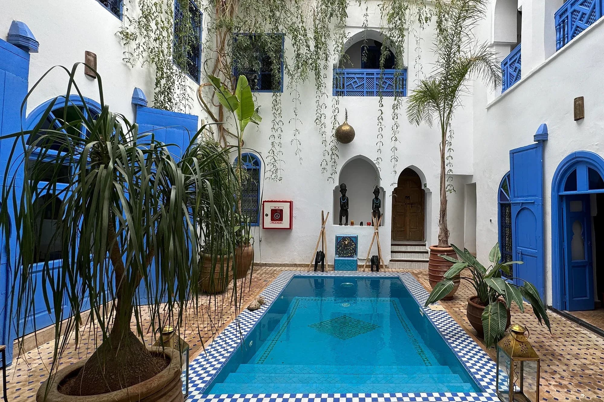 Patio de un riad de Marrakech con piscina, palmeras y puertas azules