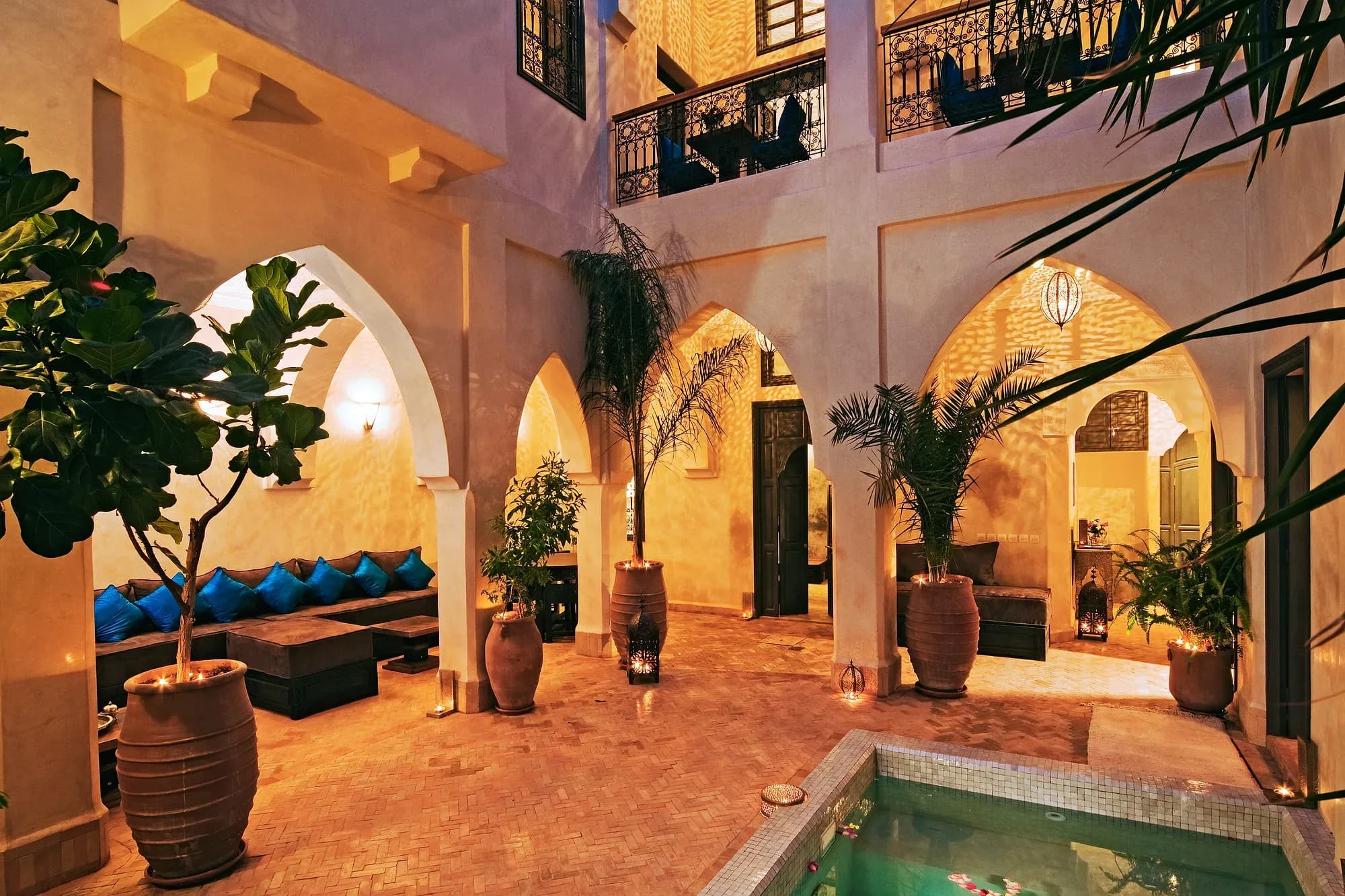 Patio de un riad de Marrakech iluminado al anochecer, con arcos, plantas y pequeña alberca