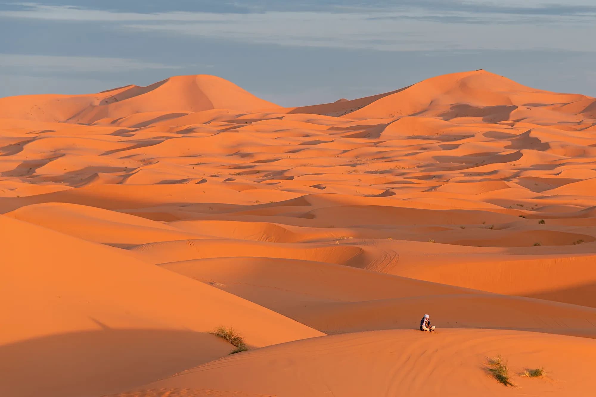 Orange Erg Chebbi dunes in afternoon light with a small figure sitting on the sand