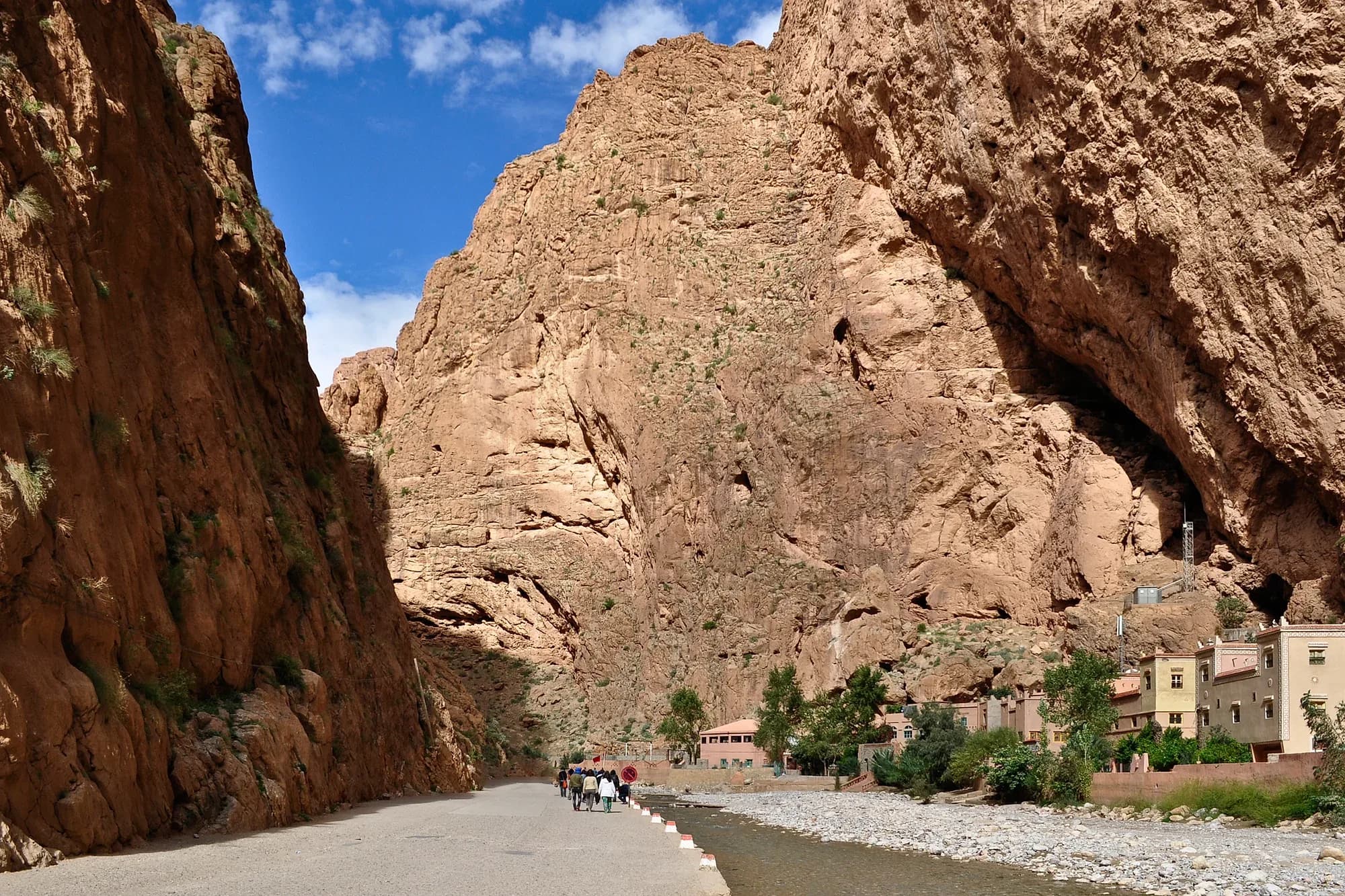 Riverbed between the high walls of the Todra Gorge, with palm trees and houses behind