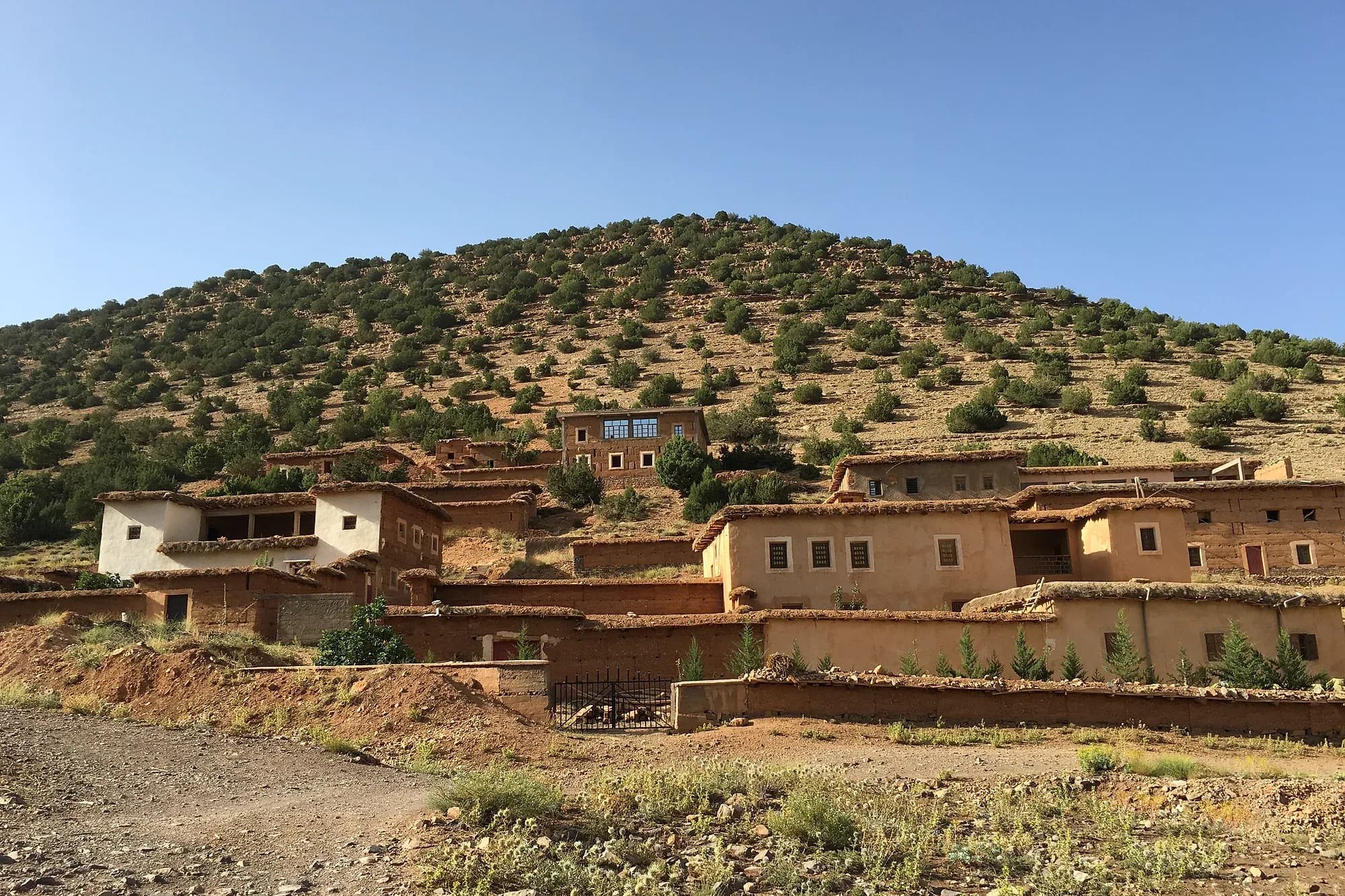 Casas de un pueblo bereber al pie de una colina con arbustos en la provincia de Azilal