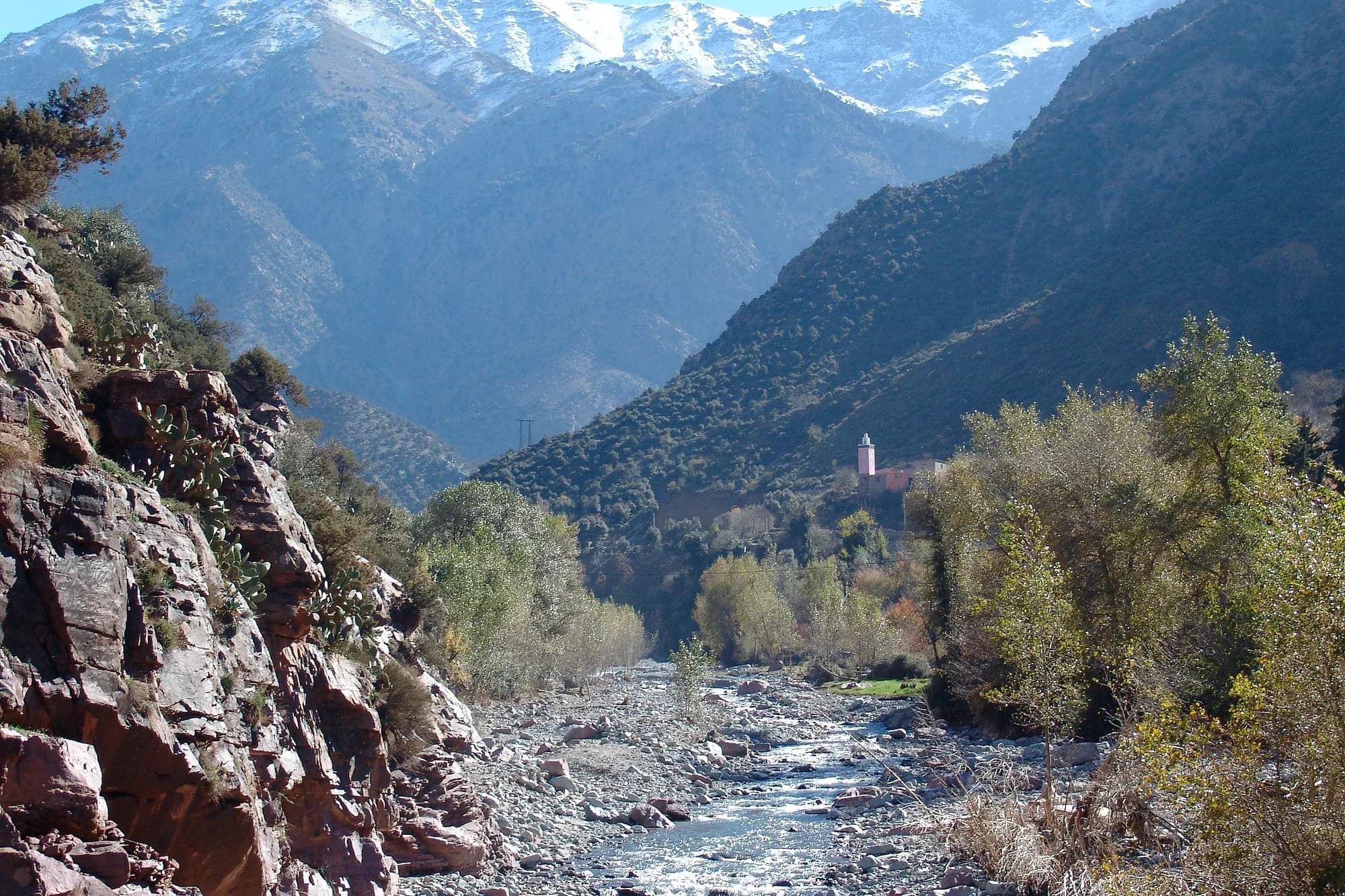 Río del valle del Ourika entre laderas arboladas con cumbres nevadas del Alto Atlas al fondo