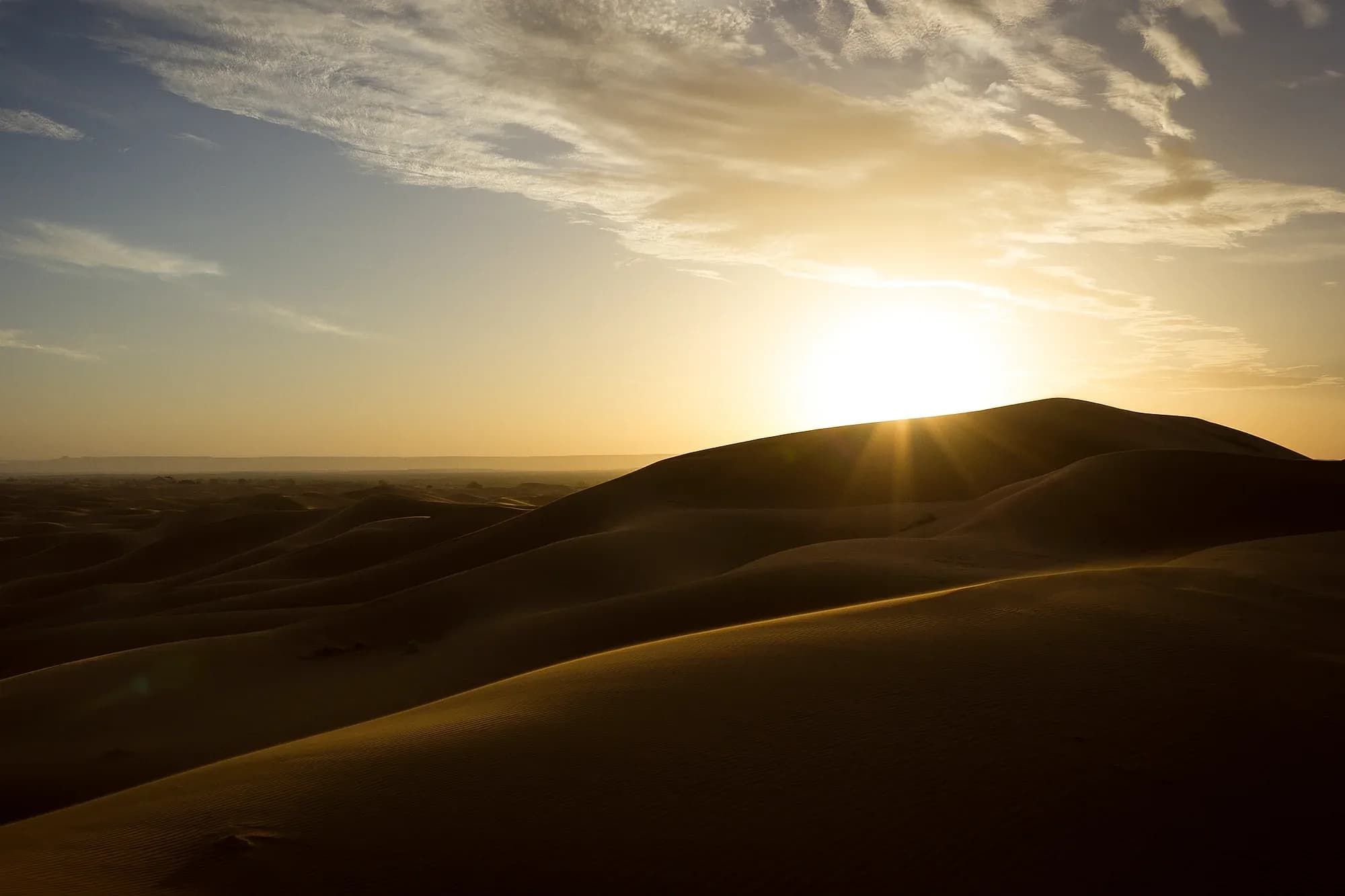 Sol naciente sobre las dunas de Erg Chebbi bajo un cielo con nubes, cerca de Merzouga