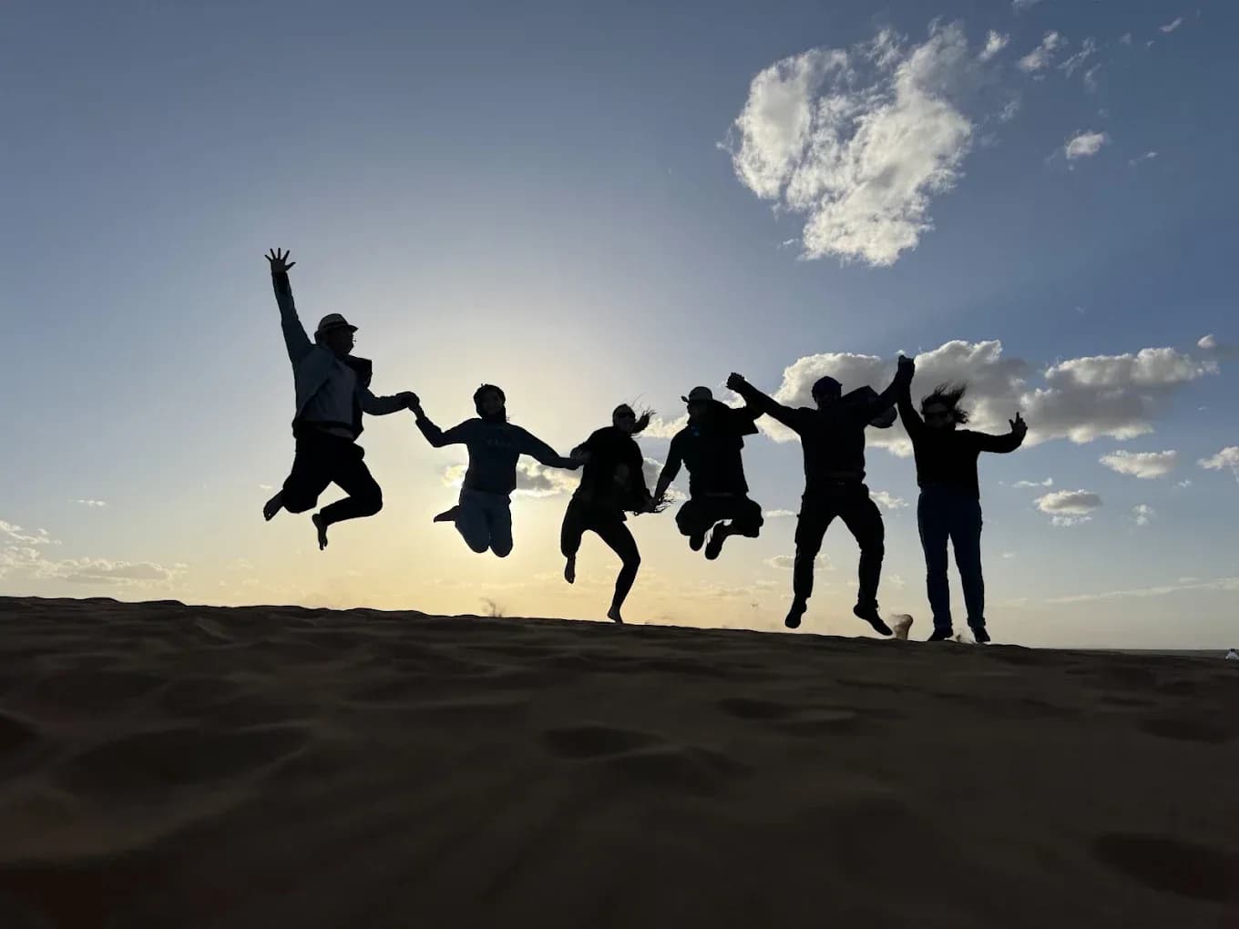 Group jumping on the dunes at sunset