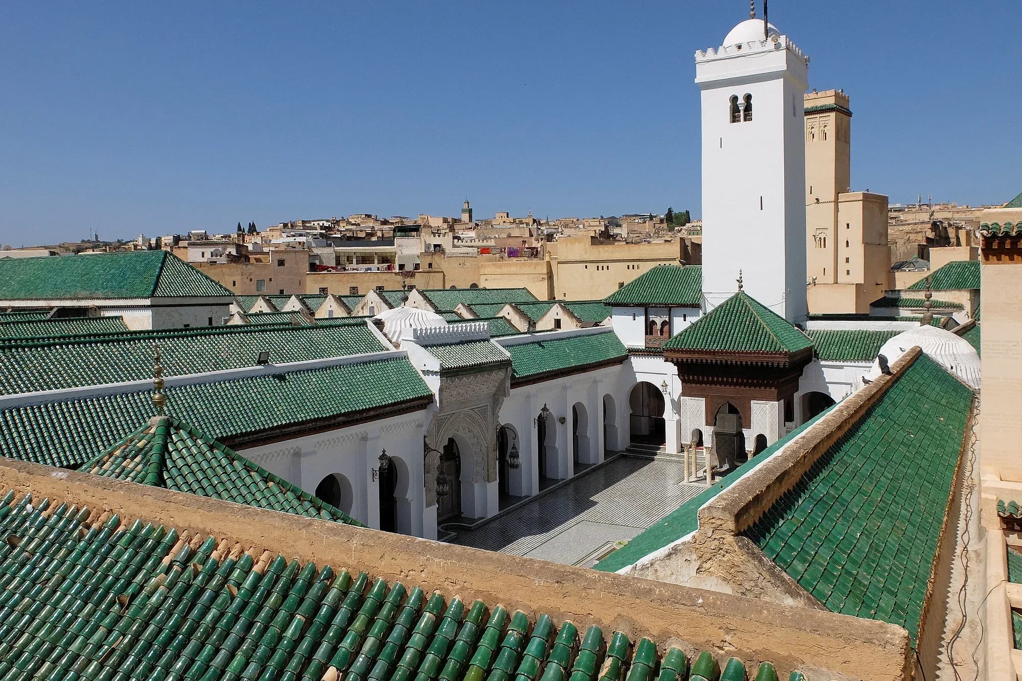 Green-tiled roofs and the minaret of Fez's Al Quaraouiyine mosque seen from a rooftop
