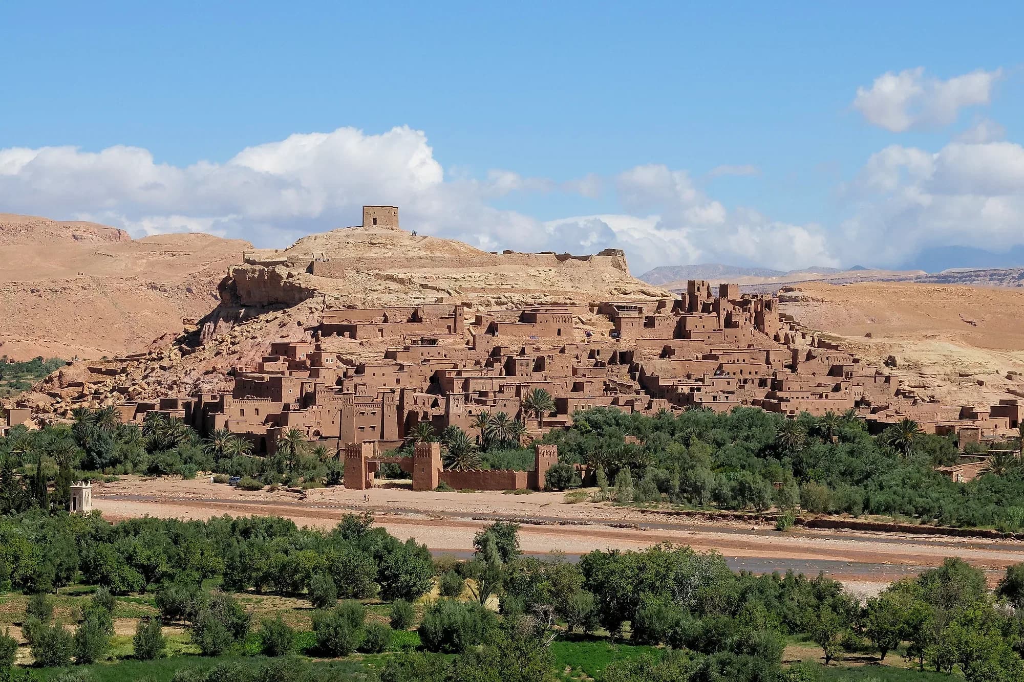 Ksar de Aït Ben Haddou sobre la colina, con el palmeral en primer plano y cielo azul