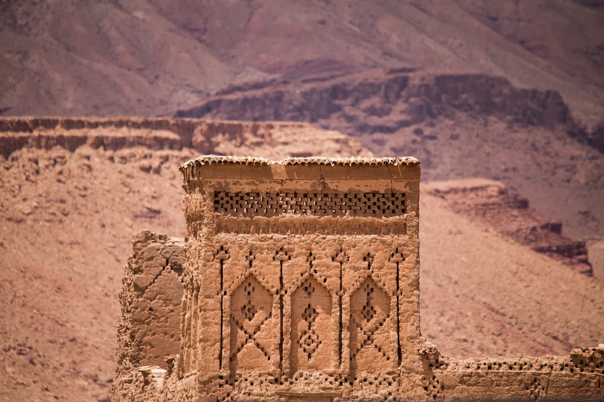 Torre decorada de una kasbah de adobe en N'Kob, con montañas áridas al fondo