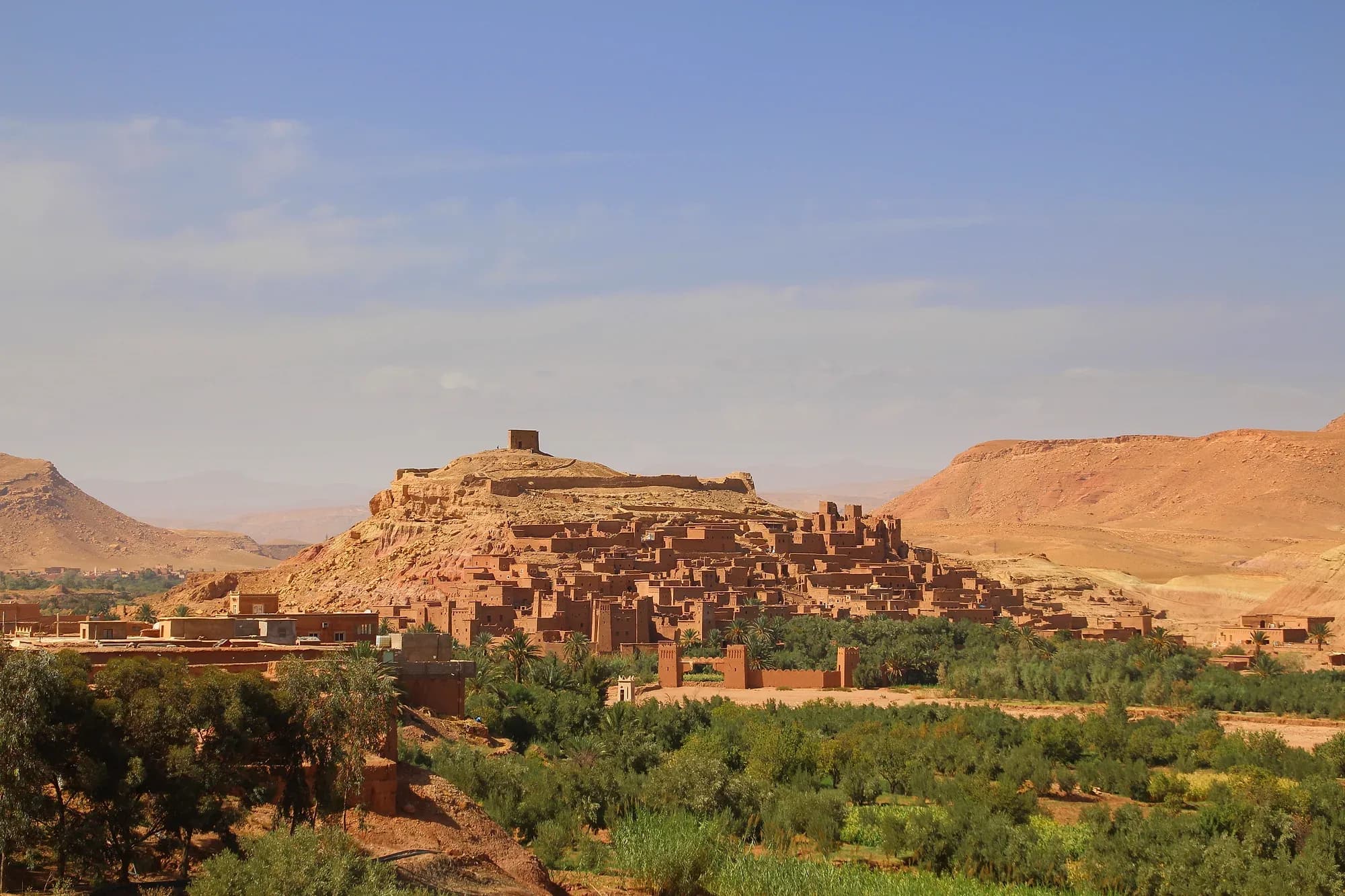 Panoramic view of the ksar of Aït Ben Haddou on its hill, with the palm grove and mountains behind