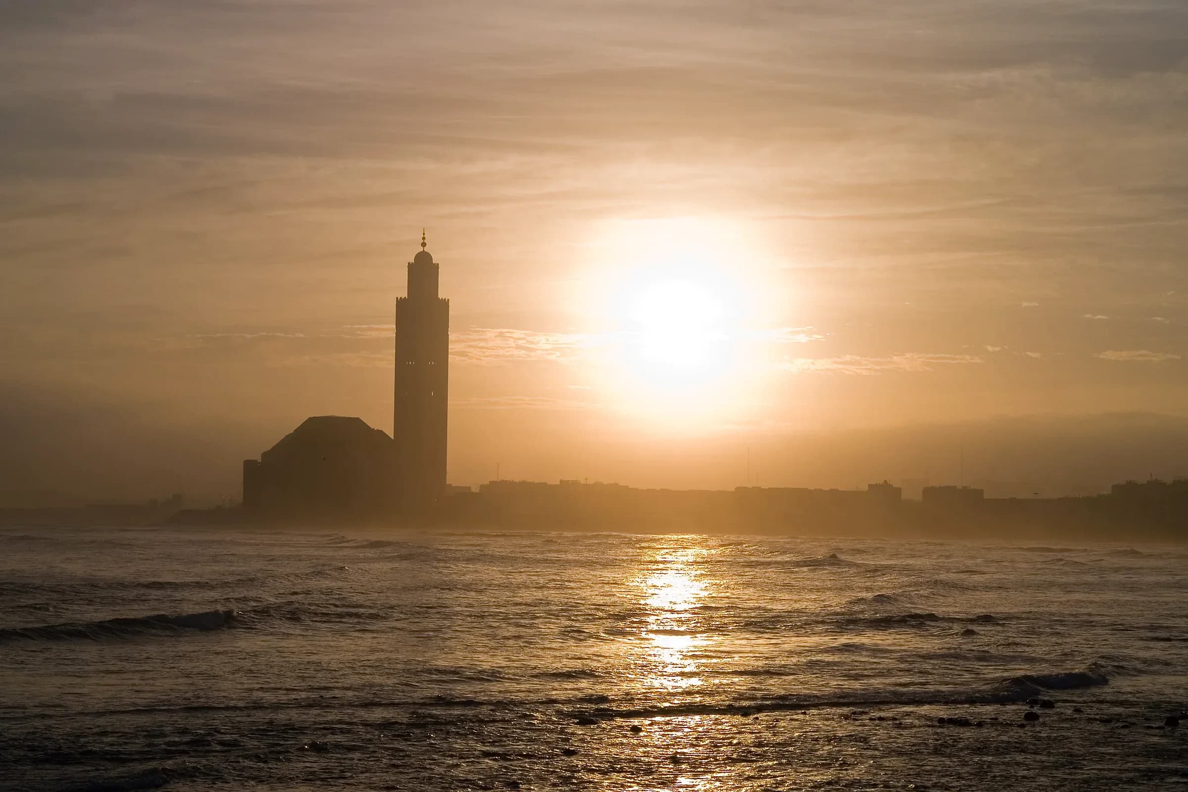 Hassan II Mosque in Casablanca at sunset, with the sun over the Atlantic Ocean