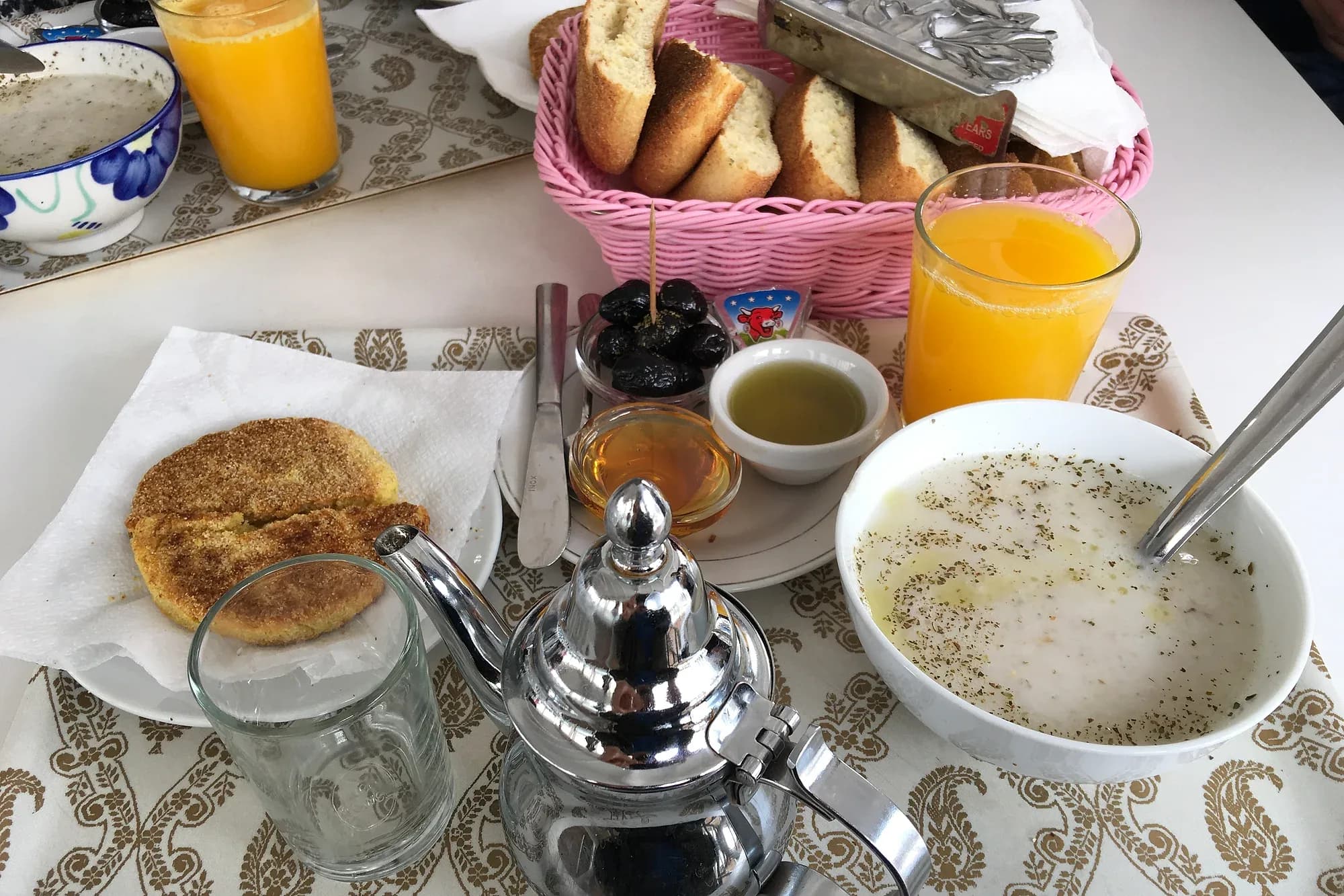 Desayuno marroquí con tetera de té a la menta, harcha, aceitunas, miel, aceite, zumo de naranja y sopa
